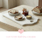 Large antique white rectangular serving board with a heart-shaped handle cut-out, featuring sourdough bread slices, jam jars, and butter on a distressed wooden table.