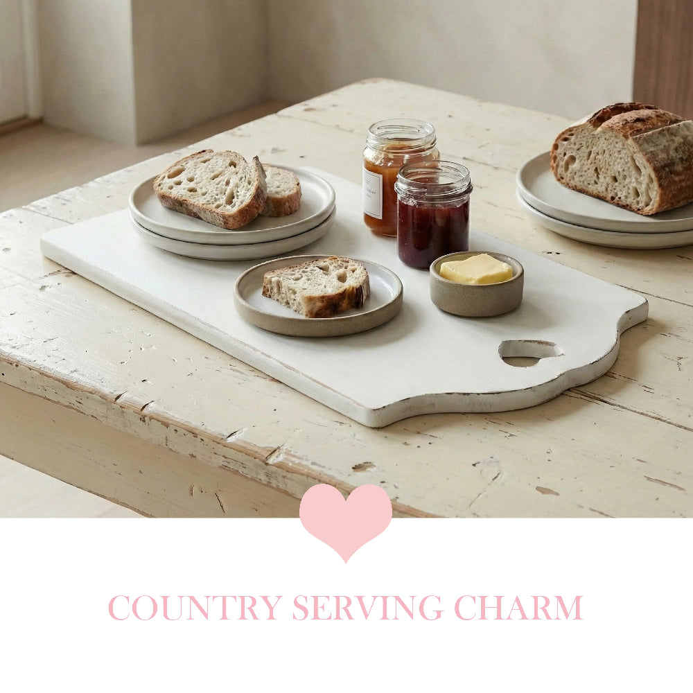 Large antique white rectangular serving board with a heart-shaped handle cut-out, featuring sourdough bread slices, jam jars, and butter on a distressed wooden table.