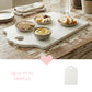 White rectangular serving board with a heart-shaped handle cutout featuring small bowls of hummus, cheese, crackers, and bread on a rustic distressed wooden table.