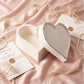 Heart-shaped box on a pink fabric background with dried flowers and a card.