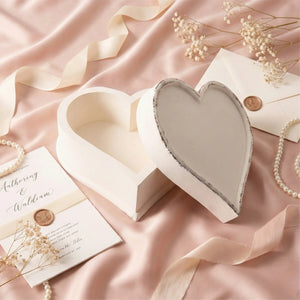 Heart-shaped box on a pink fabric background with dried flowers and a card.