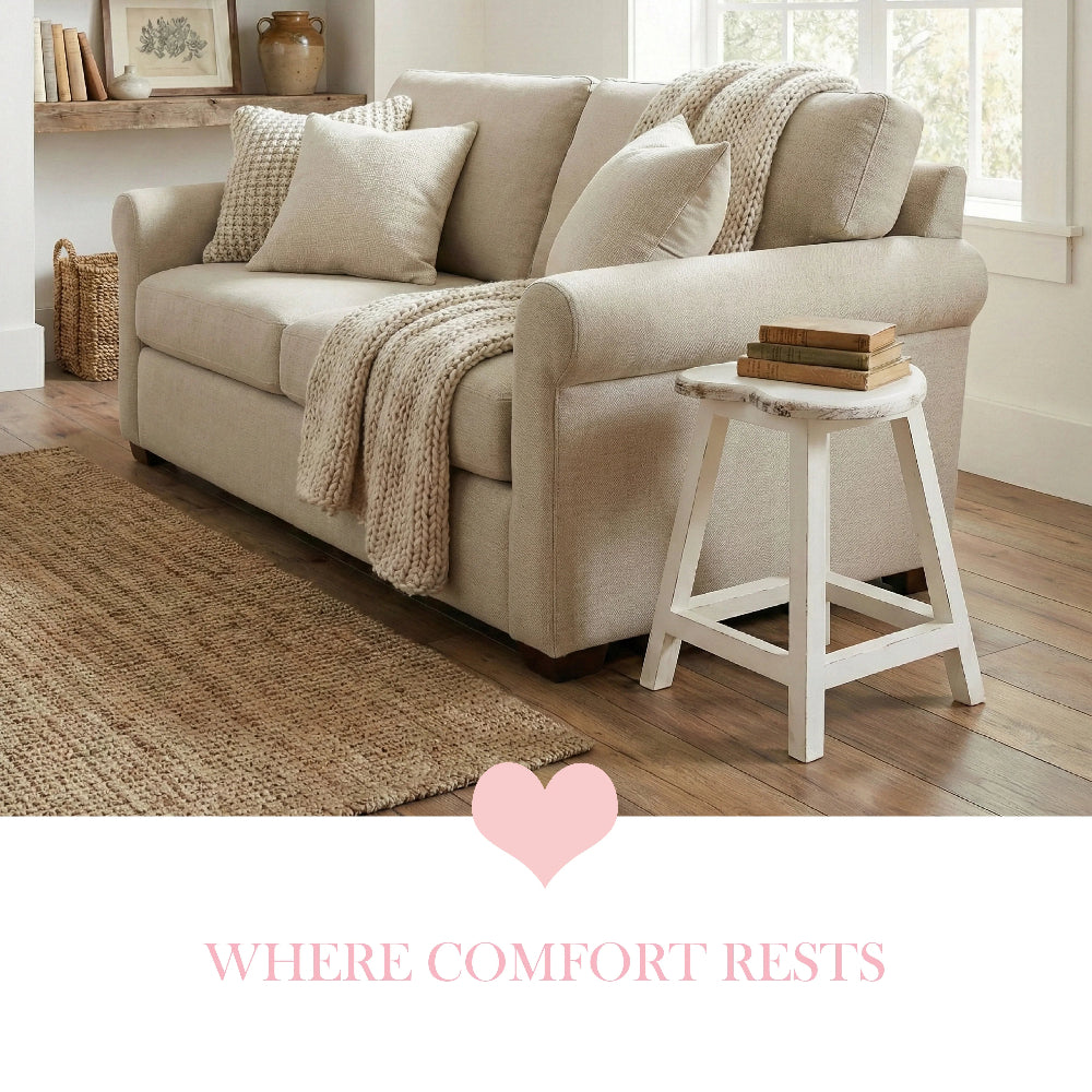 White heart-shaped stool used as a side table with books, next to a beige sofa, jute rug, and knit pillows.