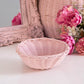 Empty pink wicker basket on white surface with pink flowers and ornate pink mirror in background