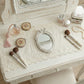Makeup vanity with decorative mirror, compact mirrors, and makeup brushes on a lace-covered surface.