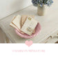 Mini Wicker Basket pink woven holding vintage books and postcards on wooden table with floral vase