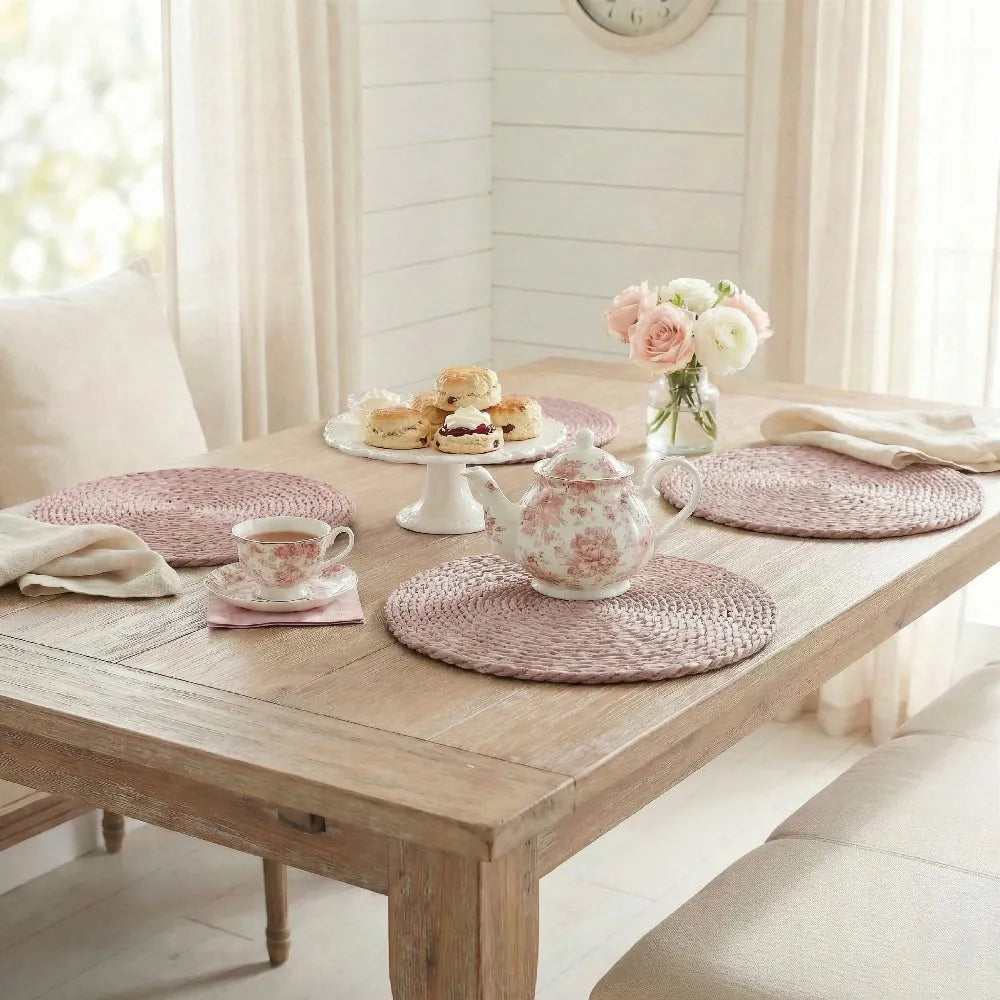 Wooden table set with tea service and pink placemats in a bright room.