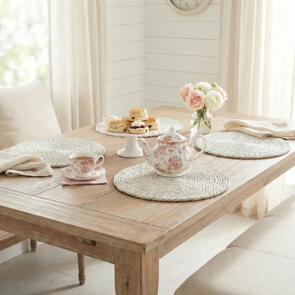 Wooden table set with teacup, teapot, and decorative items in a bright room.