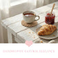 Cup of tea with a croissant and jar of jam on a wooden table, with 'Handwoven Natural Elegance' text.
