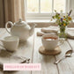 White teapot and cups on a wooden table with a vase of flowers, featuring 'Timeless Durability' text.