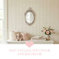 Oval ornate mirror above a dresser with fabric baskets, plush bunny, folded towels, and pink roses in a vase.