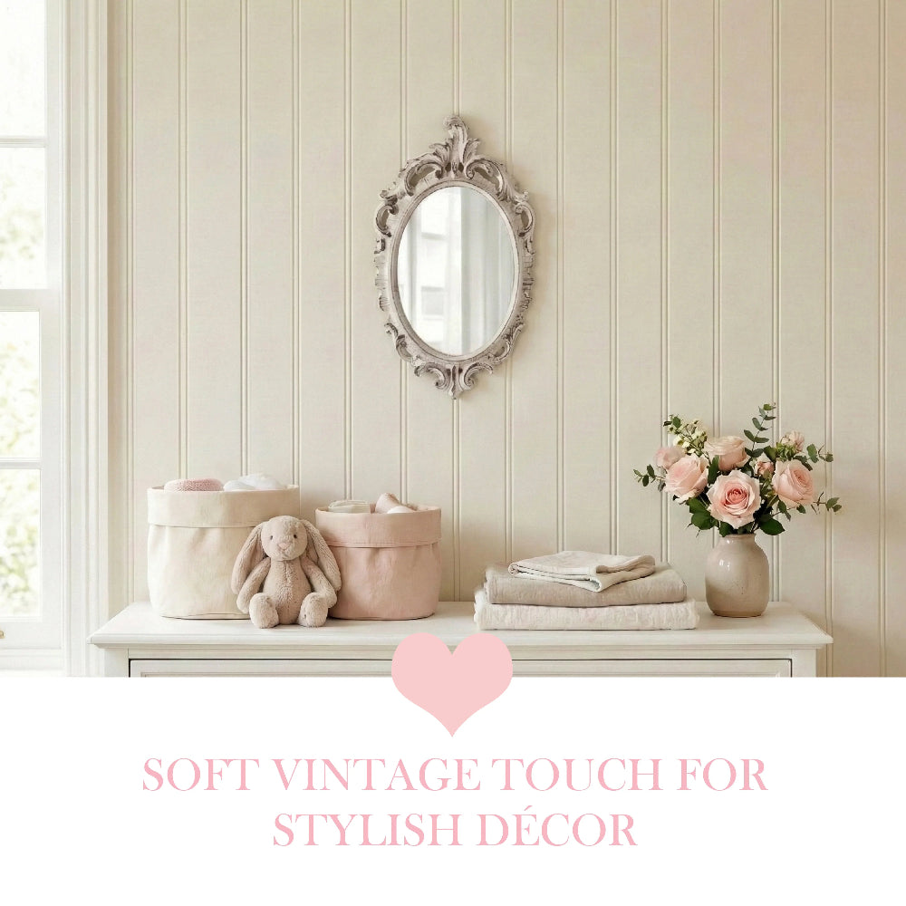 Oval ornate mirror above a dresser with fabric baskets, plush bunny, folded towels, and pink roses in a vase.