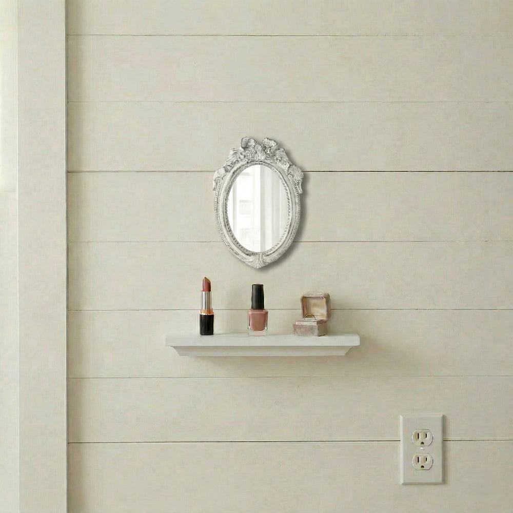 Ornate white oval mirror above a shelf with lipstick, nail polish, and a ring box on a cream shiplap wall.