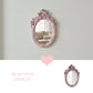 Ornate pink oval mirror on a white shiplap wall reflecting a couch, with a heart icon and Beauty in Display text.