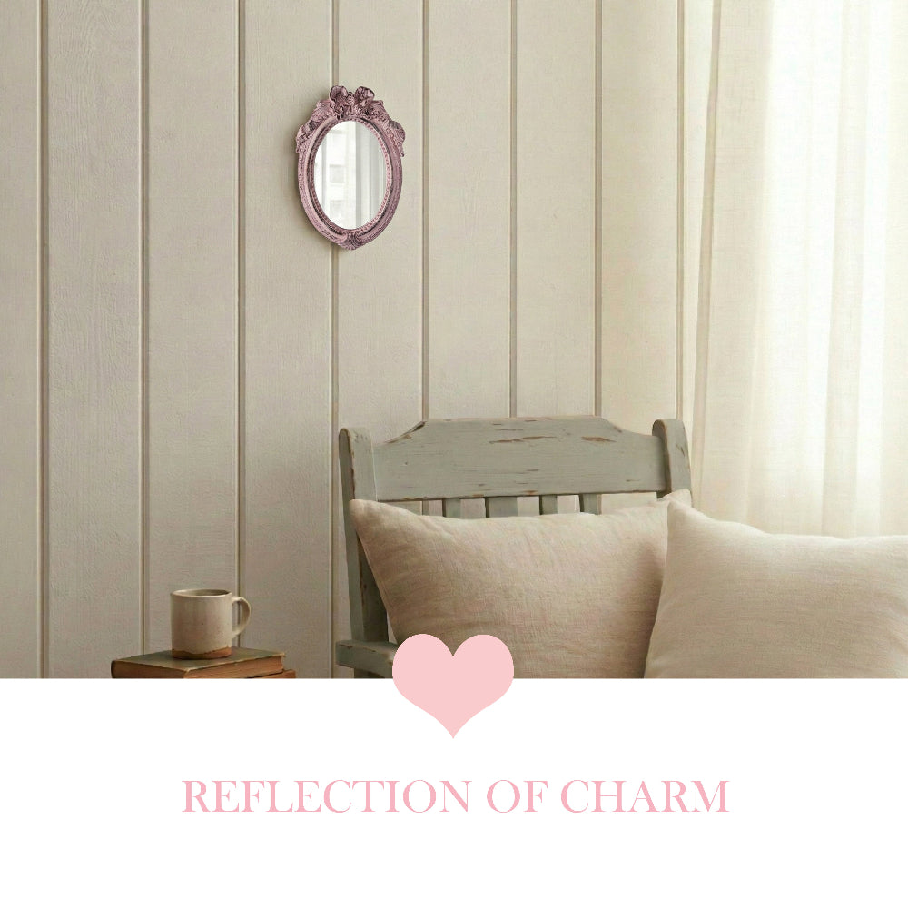 Ornate pink oval mirror on a white paneled wall above a vintage chair with pillows and a mug on stacked books.