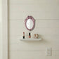 Ornate pink oval mirror on a white shiplap wall above a small shelf with lipstick, nail polish, and a jewelry box.