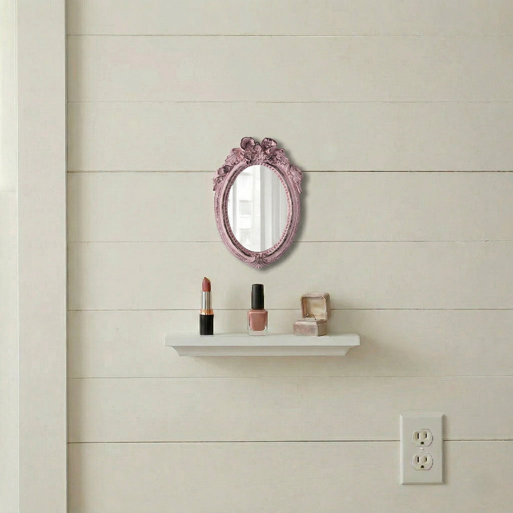 Ornate pink oval mirror on a white shiplap wall above a small shelf with lipstick, nail polish, and a jewelry box.
