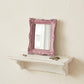 Ornate pink rectangular mirror on a white floating shelf with vintage keys and a small dried flower.