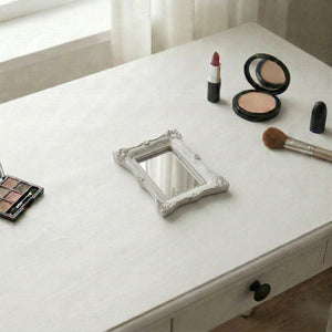 Small ornate rectangular mirror on a white vanity desk with an eyeshadow palette, lipstick, and makeup brush.