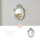 Ornate white oval mirror on a white shiplap wall reflecting a couch, with a pink heart and Beauty in Display text.