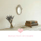 Ornate white oval mirror on a white wood vanity next to makeup brushes, lipstick, and a gold compact.