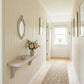 Ornate oval mirror above a wooden wall shelf with a flower vase in a hallway with shiplap walls and a jute runner.