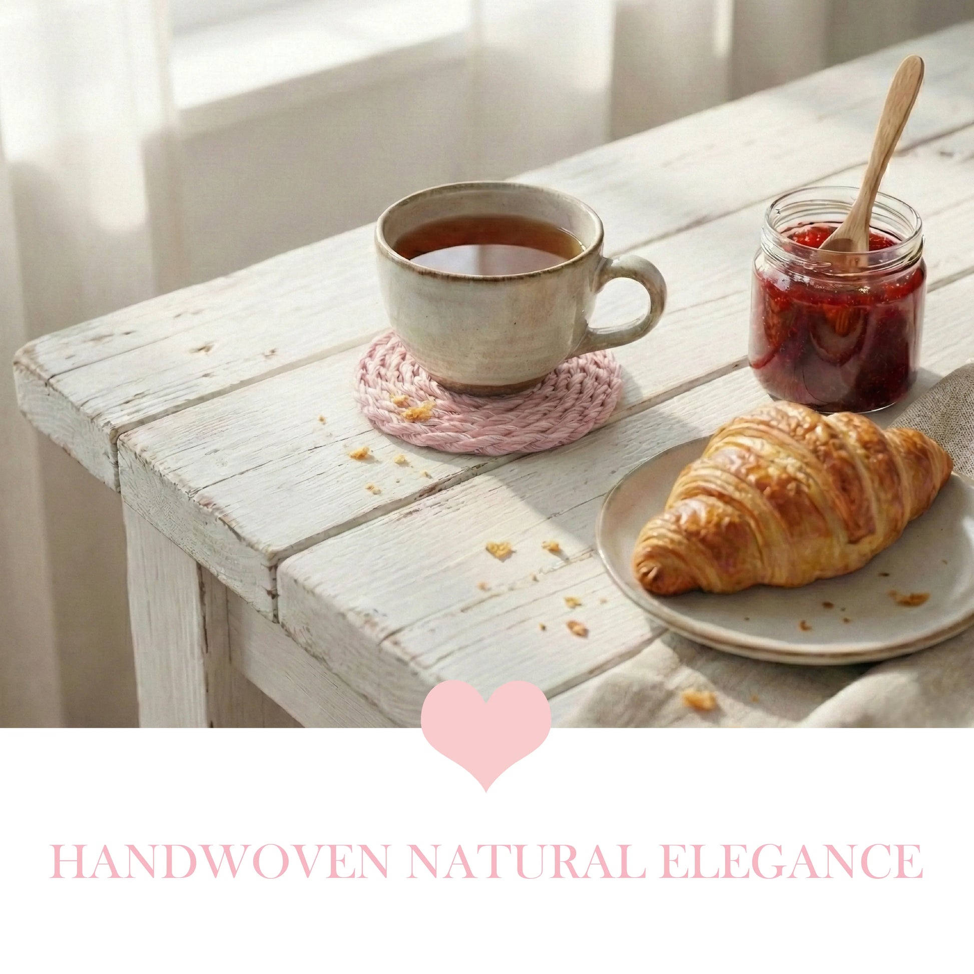 Pale pink woven coaster with a tea mug, croissant, and jam jar on a distressed white wooden table by a window.