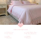 Pale pink ruffled bedding on a white bed frame with a matching ruffled cushion and two standard pillows.