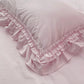 Close-up of a pale pink pillow featuring a double-layered ruffled border resting on matching bed sheets.