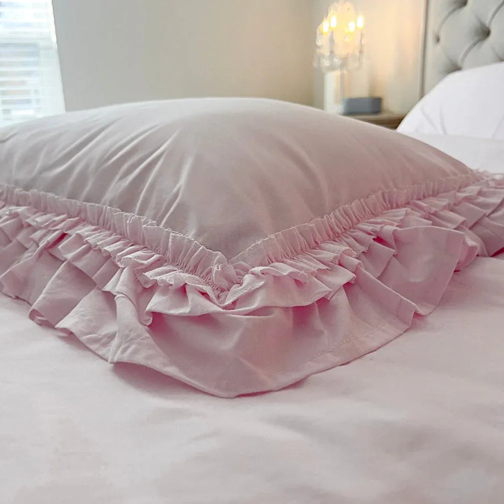 Close-up of a pale pink ruffled pillowcase on a bed with a warm crystal lamp glowing in the background.