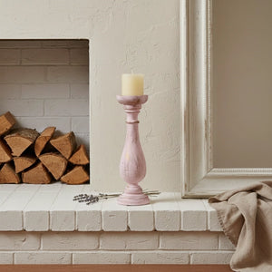 Pink candle holder on a fireplace mantle with a candle and dried lavender.