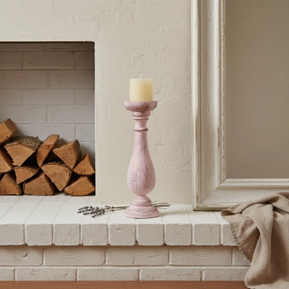 Pink candle holder on a fireplace mantle with a candle and dried lavender.