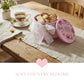 Pink cookie tin with lace bow on a wooden table with tea and cookies, 'Soft Country Blooms' text.