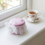 Pink decorative box with floral design on a windowsill next to a cup of tea.