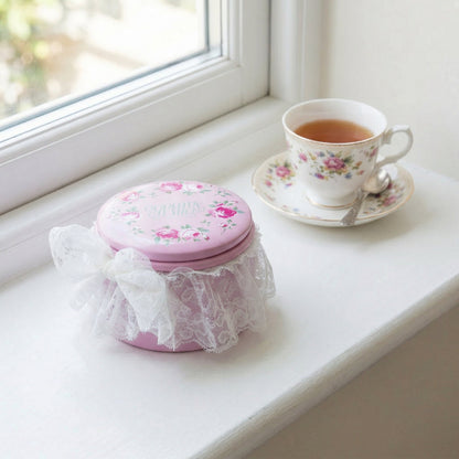 Pink decorative box with floral design on a windowsill next to a cup of tea.