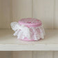 Pink decorative jar with floral lid and lace on a wooden shelf
