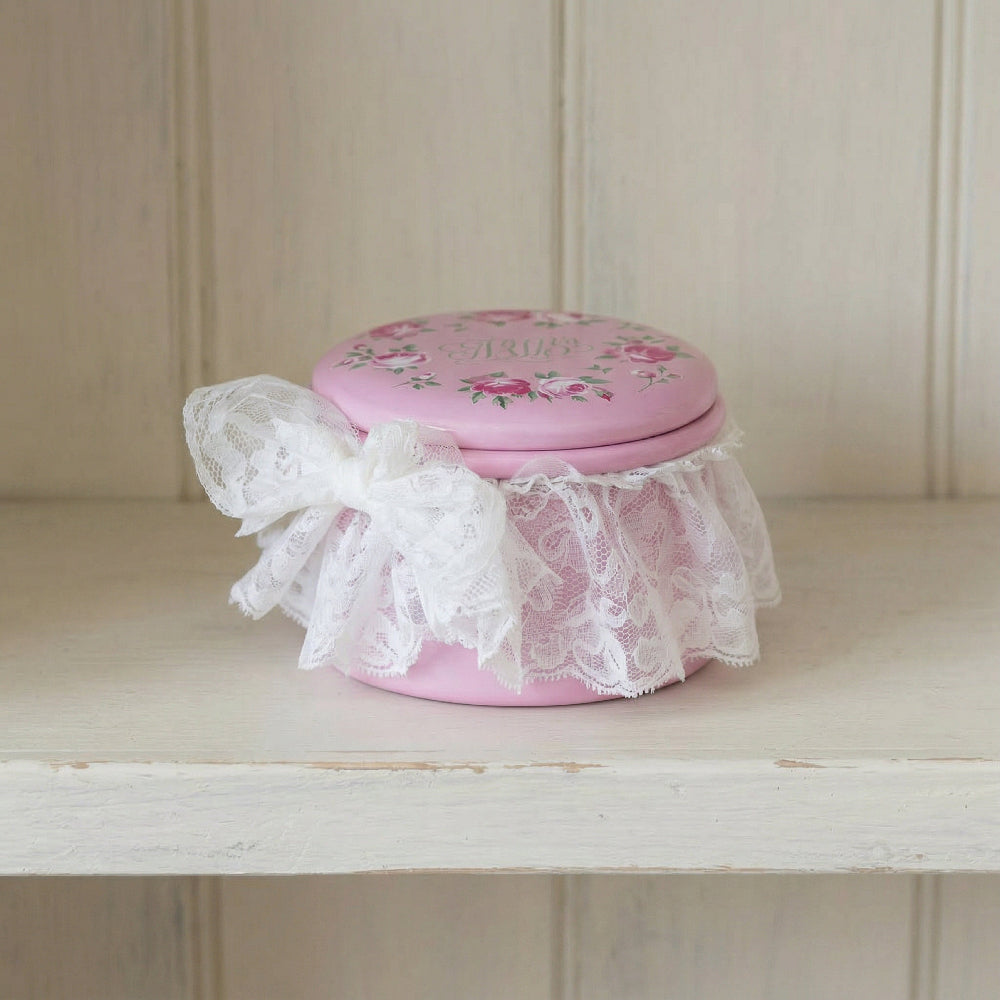 Pink decorative jar with floral lid and lace on a wooden shelf