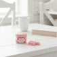 Pink jar with a lid on a white surface with a blurred background


