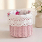Small pink wicker basket with a white rose-patterned fabric lining and crochet lace trim on a white surface.