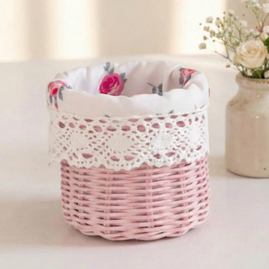 Small pink wicker basket with a white rose-patterned fabric lining and crochet lace trim on a white surface.