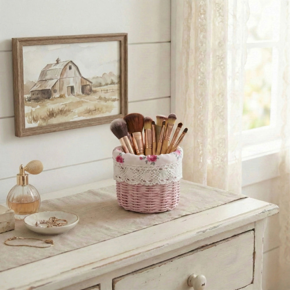 Pink mini wicker basket holding makeup brushes on a white dresser next to jewelry and a barn picture.