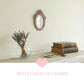 Small pink ornate mirror on a wall above a table with dried lavender, vintage books, a magnifying glass, and a heart.