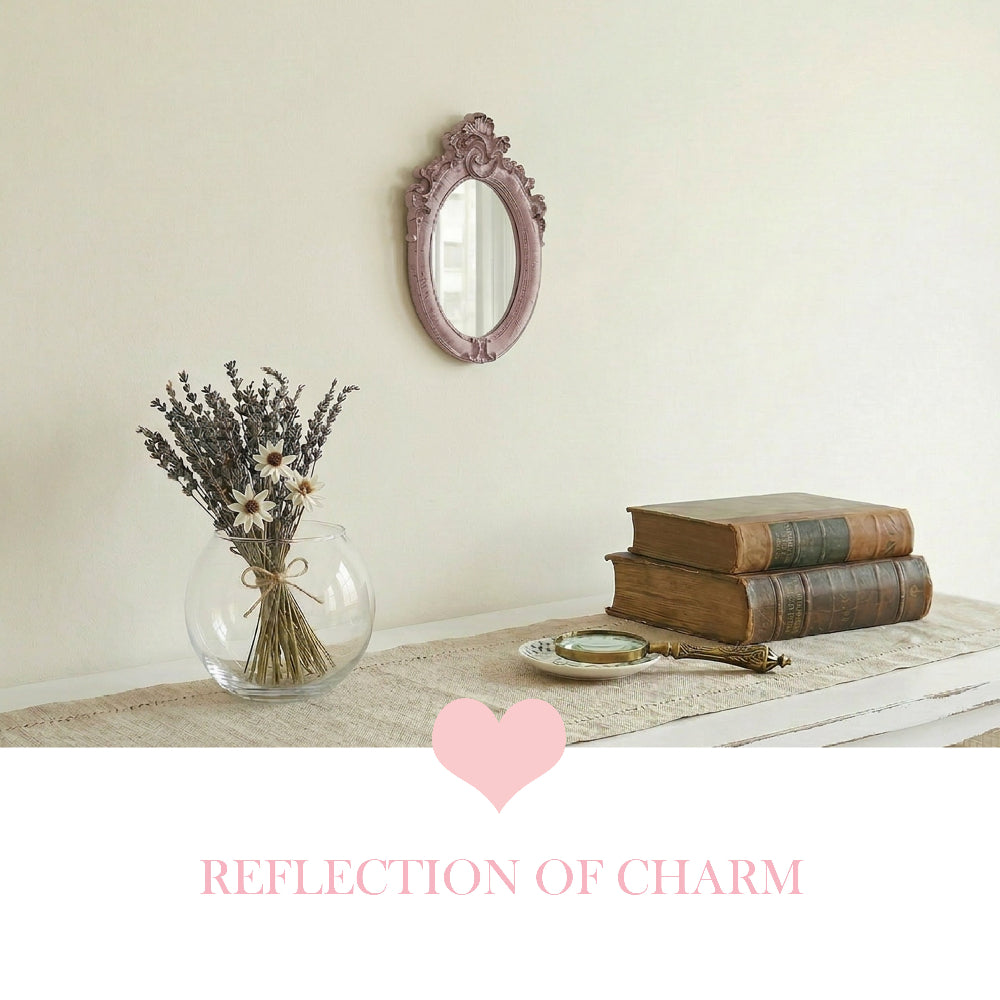 Small pink ornate mirror on a wall above a table with dried lavender, vintage books, a magnifying glass, and a heart.