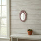 Small pink oval ornate mirror on a white wood plank wall above a white table with a small potted succulent.