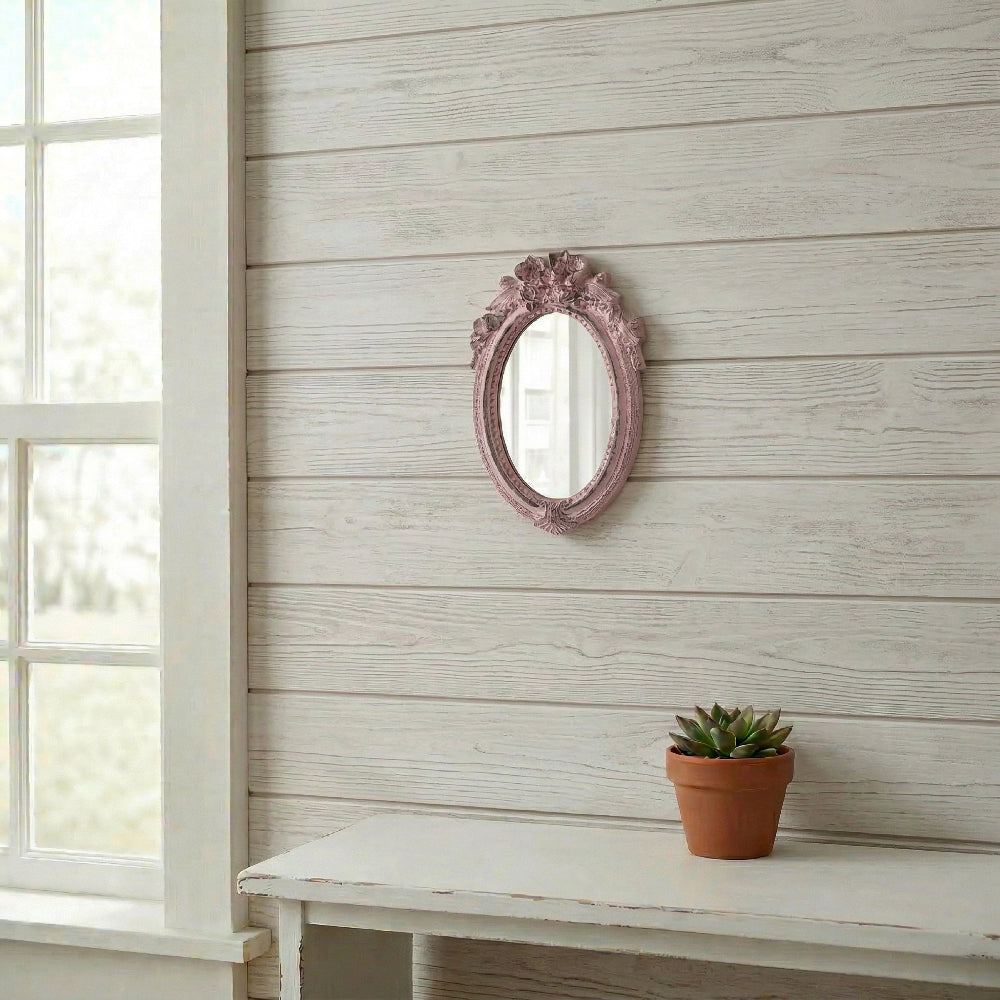 Small pink oval ornate mirror on a white wood plank wall above a white table with a small potted succulent.