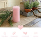 Lit pink pillar candle on a wooden tray with lavender, a heart stone, and a pitcher of roses on a bed.