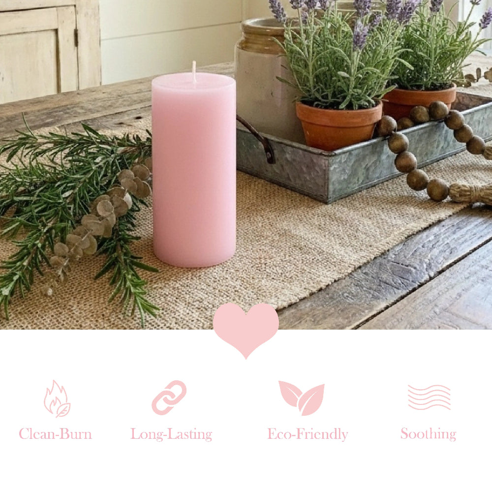 Lit pink pillar candle on a wooden tray with lavender, a heart stone, and a pitcher of roses on a bed.