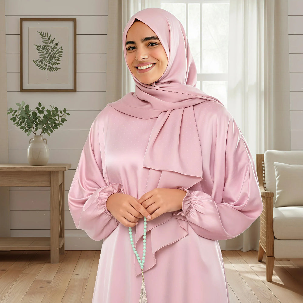 Woman in a pink polka dot Isdal prayer dress holding green beads in a bright living room.