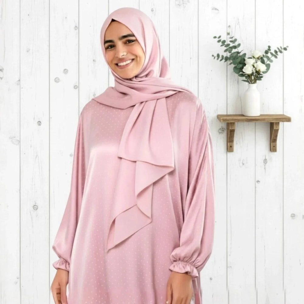 Woman wearing a pink hijab and polka dot Isdal Prayer dress against a white wooden background