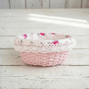 Pink wicker basket with floral lace linen on a wooden surface
