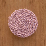 Pink woven coaster on a wooden surface.